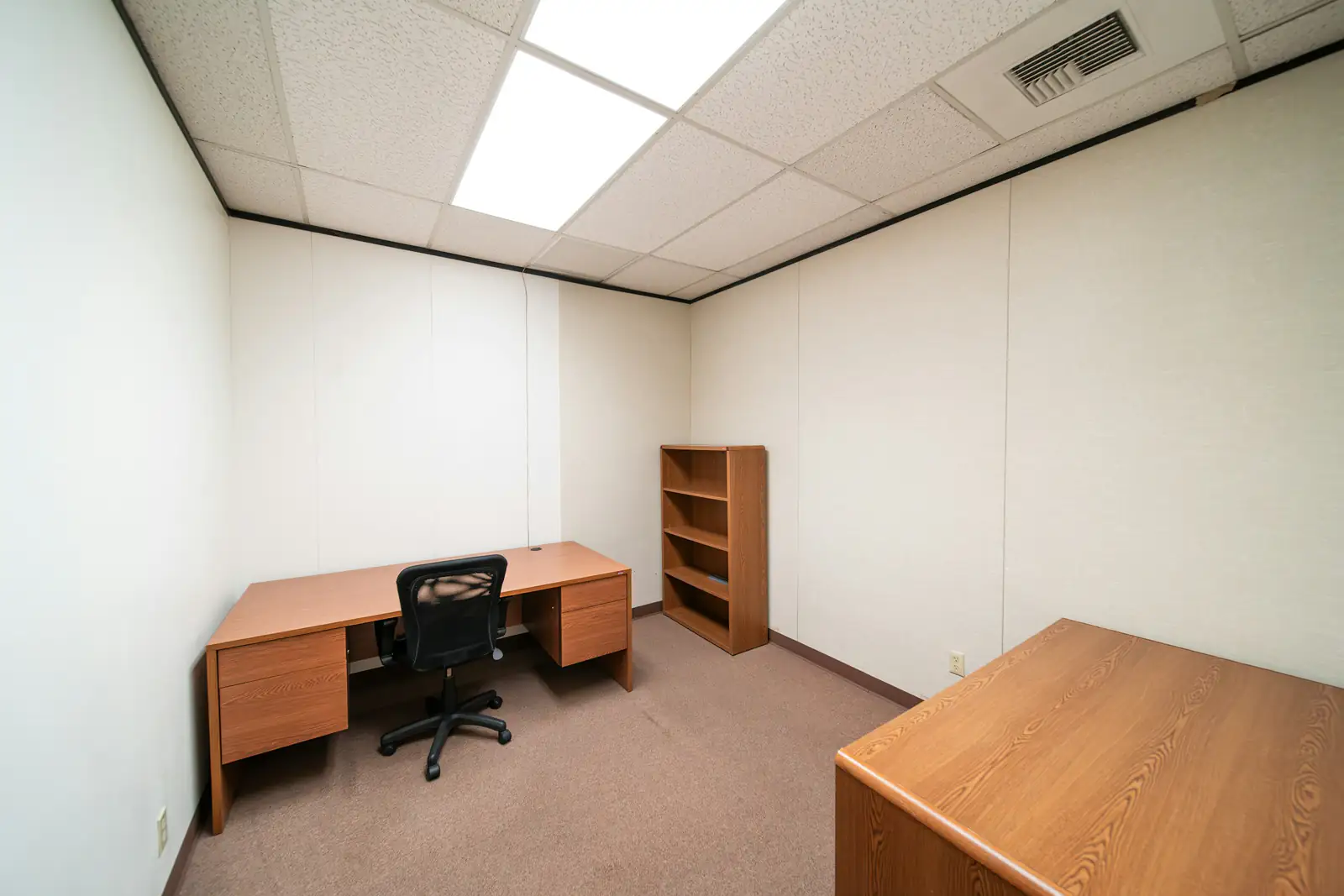 Ausgeräumtes Büro mit Schreibtisch, Bürostuhl und leerem Regal