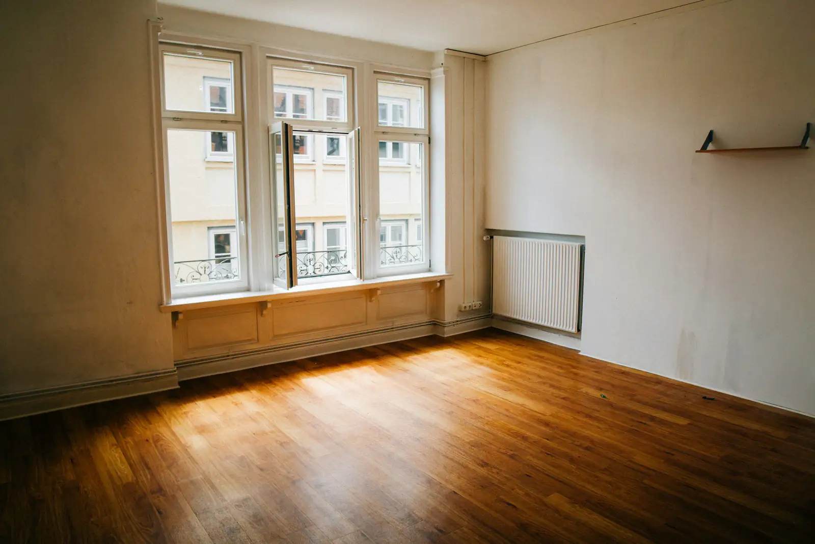 Leerer, heller Altbau-Raum mit Holzboden, hohen Sprossenfenstern und Heizkörper