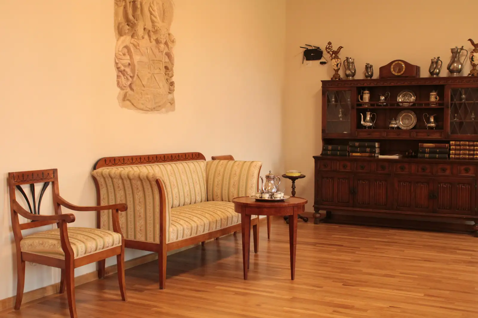 Wohnzimmer mit gestreiftem Sofa, Holzstuhl, rundem Beistelltisch und Vitrinenschrank